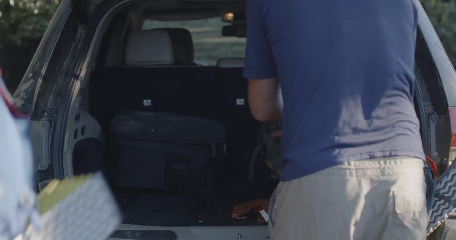 A man opens the back of an suv and he and a friend take out backpacks