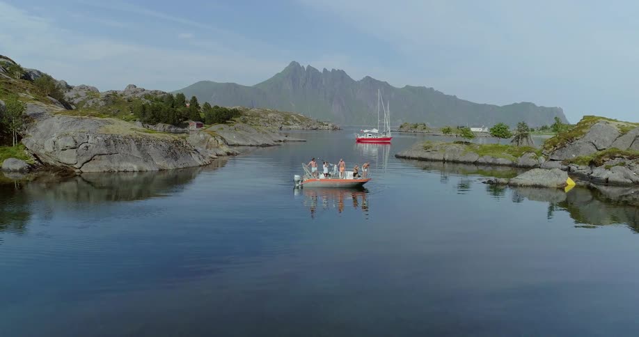 A small boat with many people in it sailing in a calm body of water with mountains and another boat in the background