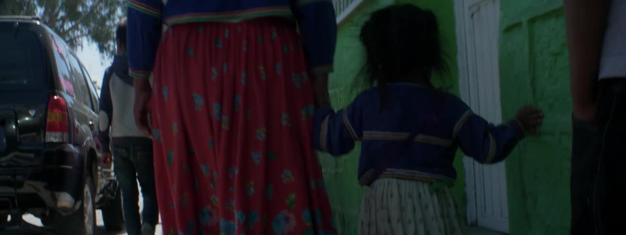 Woman in a red skirt walks down a sidewalk while holding a child's hand