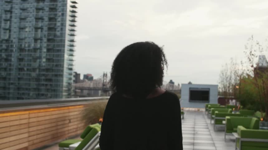 Woman walks across a rooftop with large buildings on her side