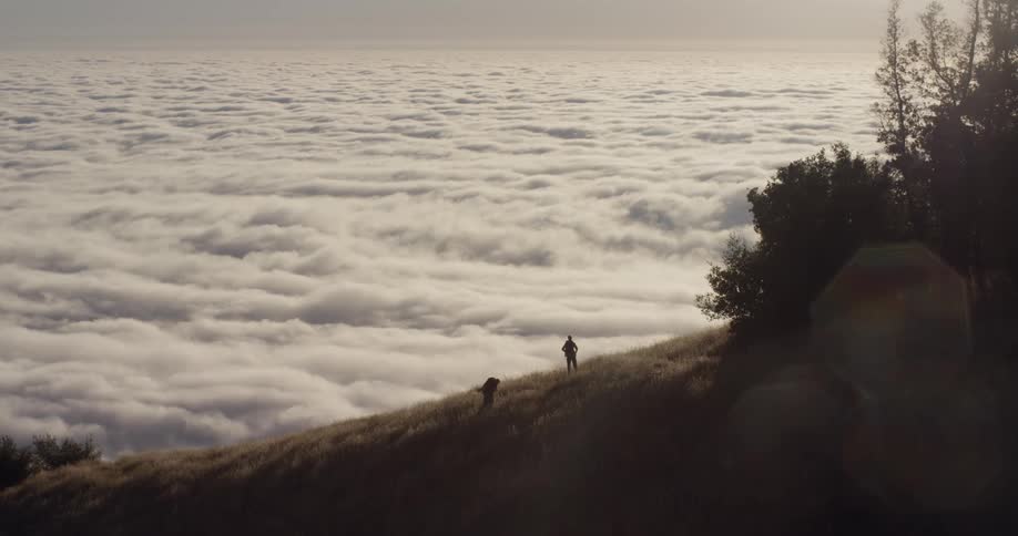 Two people are hiking uphill over the clouds