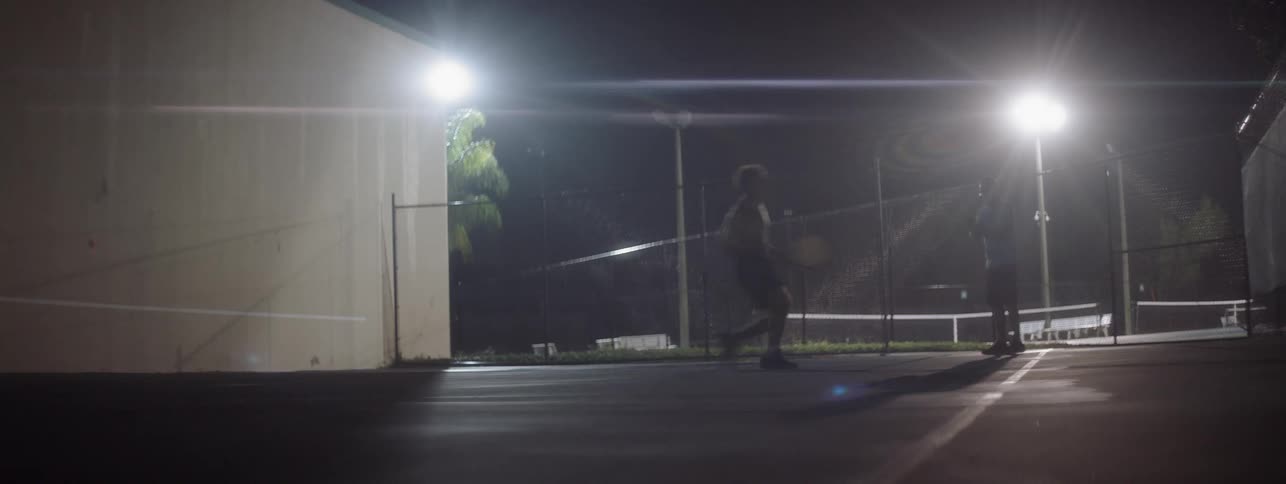 Man plays tennis on an outdoor court at night