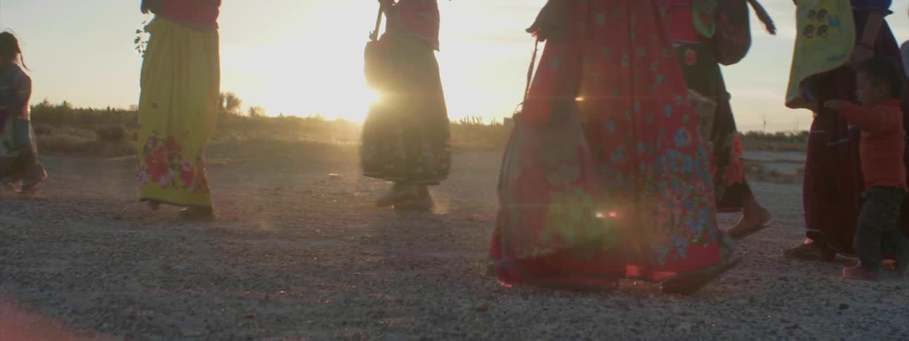 Several people walk down a dirt road at sunset