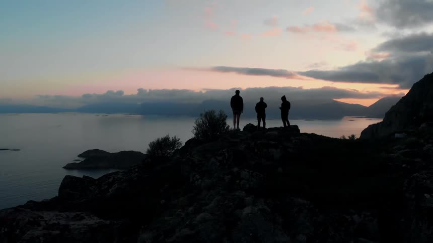 People stand on the rocks by the shore at dawn