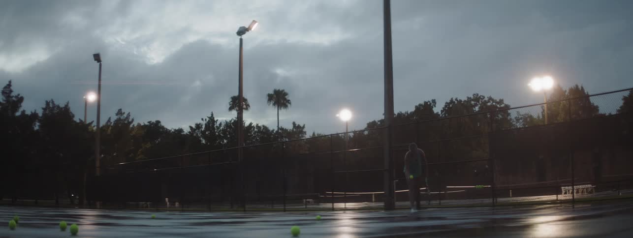 Person plays tennis on a court in the evening