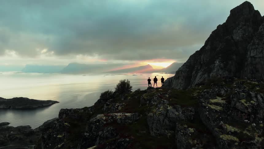 Three people stand on a cliff overlooking waer