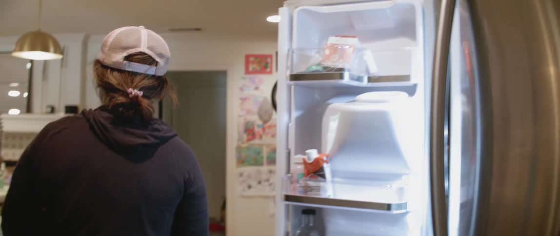 A woman removes items from the fridge and walks to the table