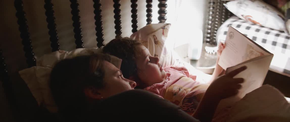 A woman reads a book in bed with her daughter
