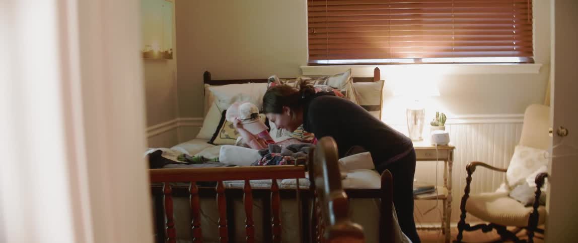 A woman plays with a child holding a hat on a bed in a bedroom