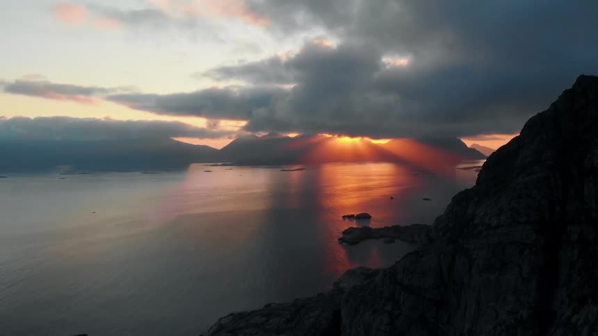 The sun is setting behind the large clouds near the water