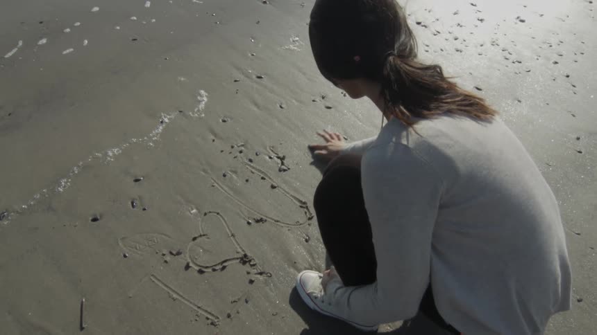 A woman writes in the sand on a beach