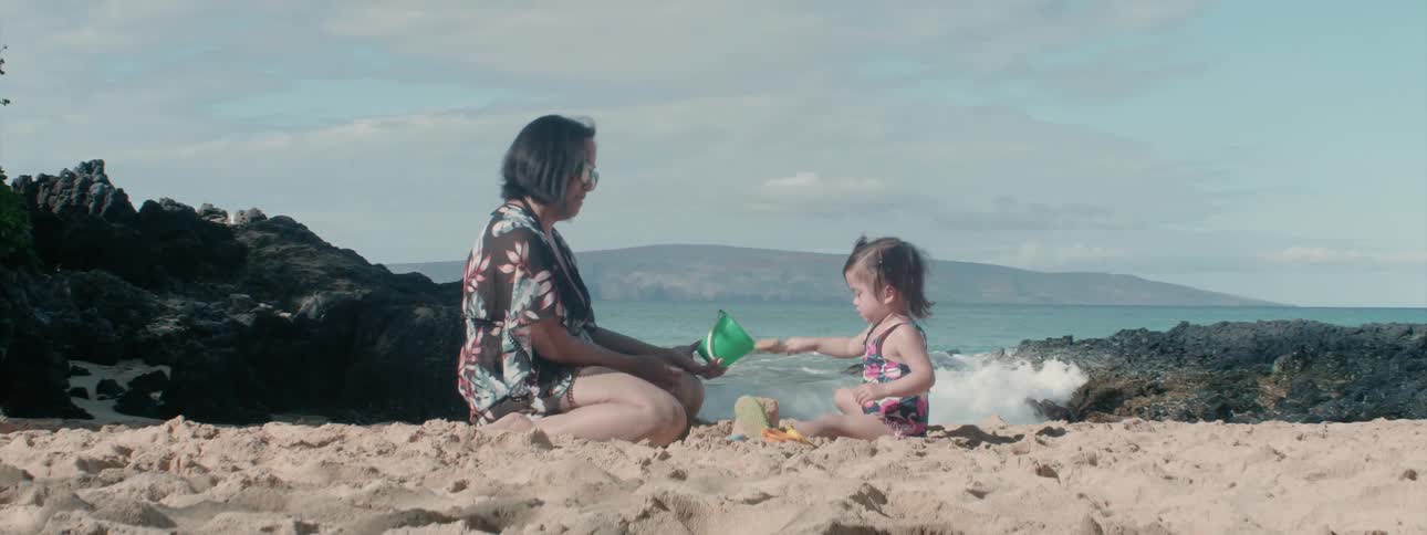 A woman builds a sand castle with a young girl
