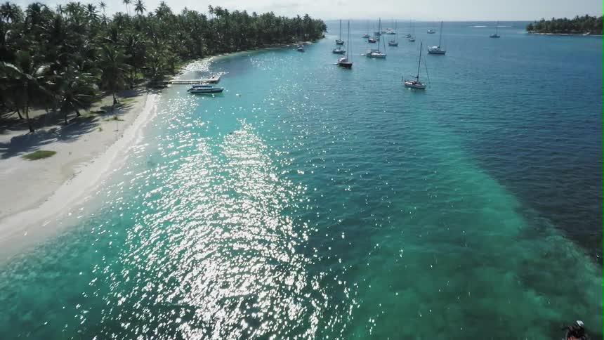 Aerial view of a clear blue beach with many boats moving and anchored