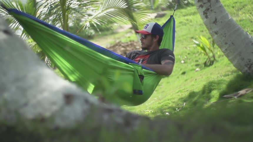 A man lays in a hammock surrounded by palm trees