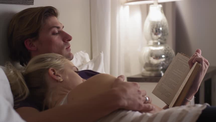A man and woman are cuddling in bed reading