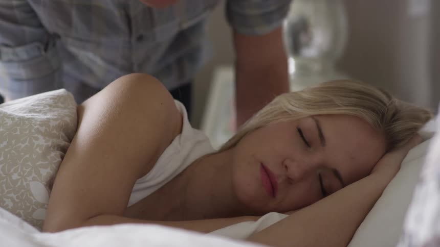 Woman sleeping in bed and man kisses her and she wakes up