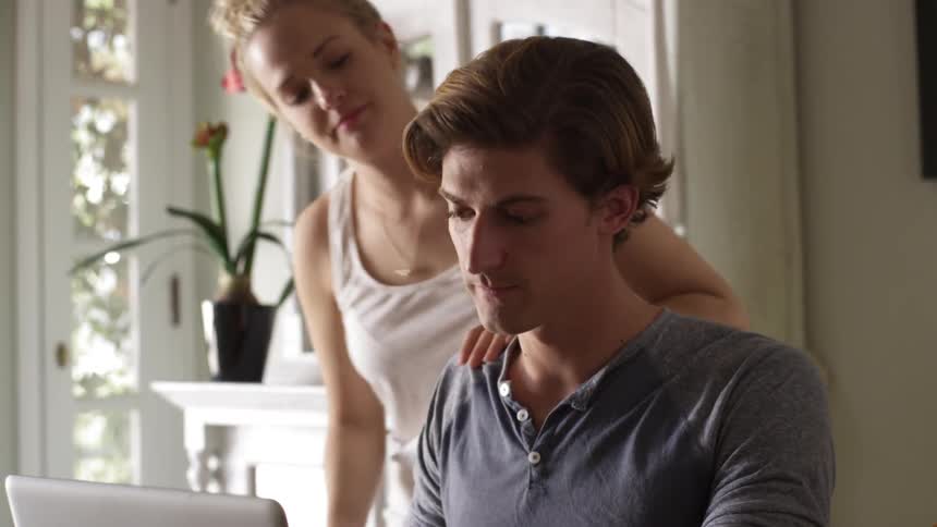 Woman comes up and hugs a man using a laptop