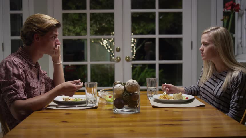 A man and woman arguing and eating dinner at a table