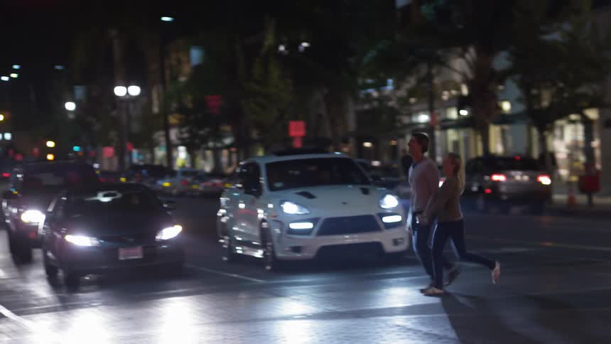 A man and woman run across a city crosswalk while holding hands