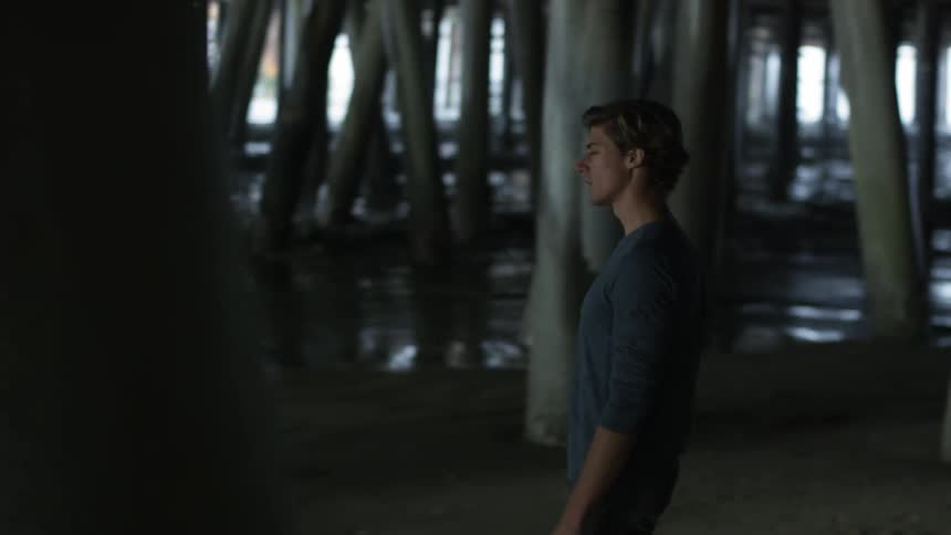 A man walking under a pier at the beach
