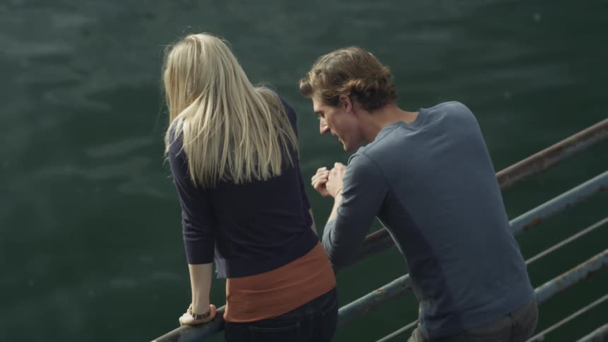 A man and a woman lean on a rail and look at the water