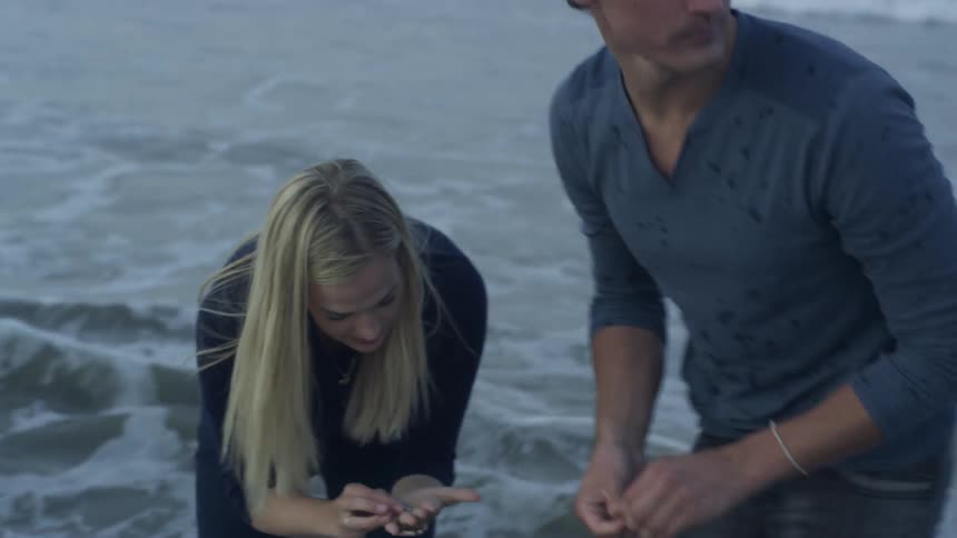 People picking up small items in the sand as the tide comes in