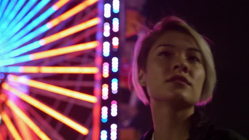 Woman looks around in a brightly lit amusement park at night