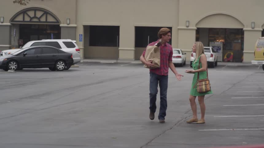 A man and woman argue as they walk through a parking lot
