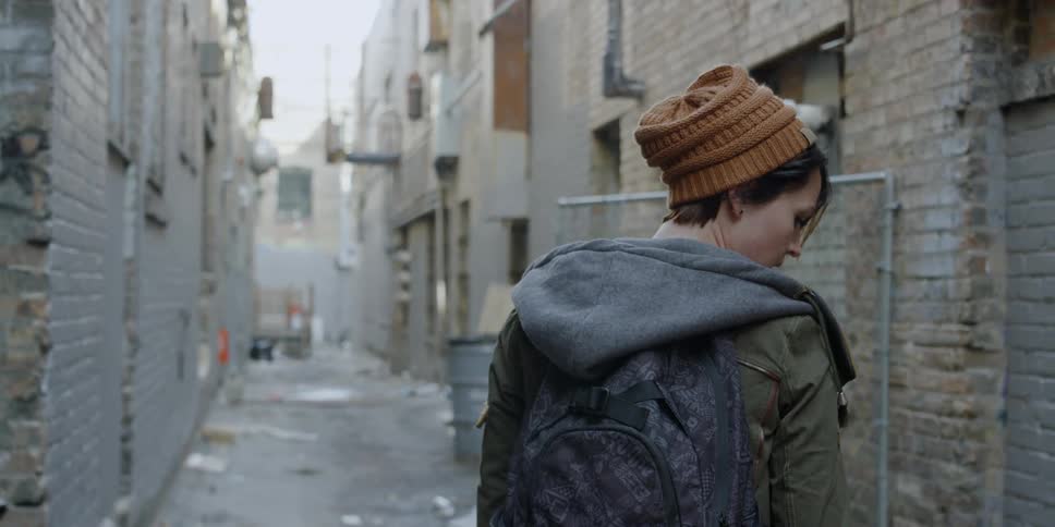 A woman looks around an alley as she walks