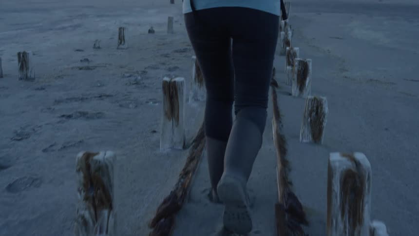 A woman is walking between piles in the sand on a beach at dusk