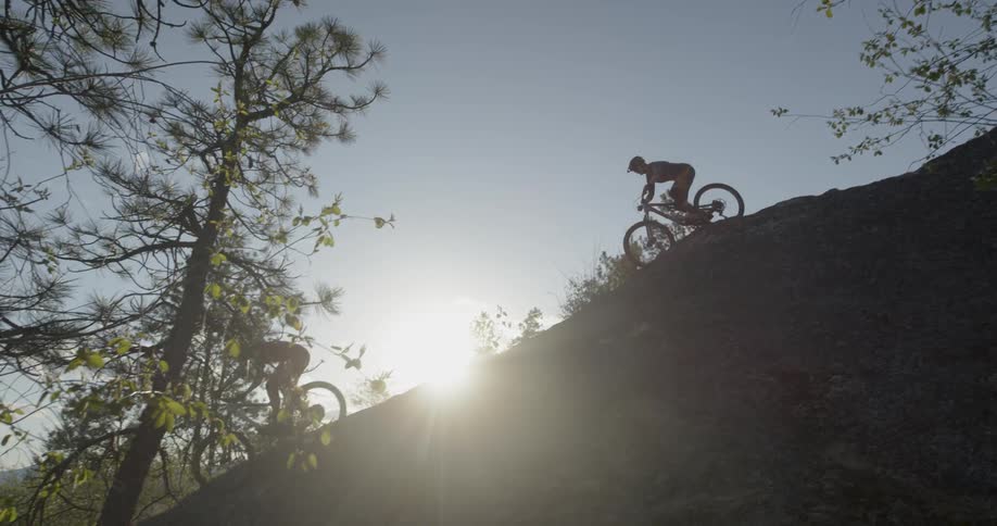 Two people ride bicycles down a hill under the bright sun
