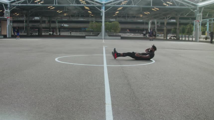 Man does sit ups on an outdoor basketball court