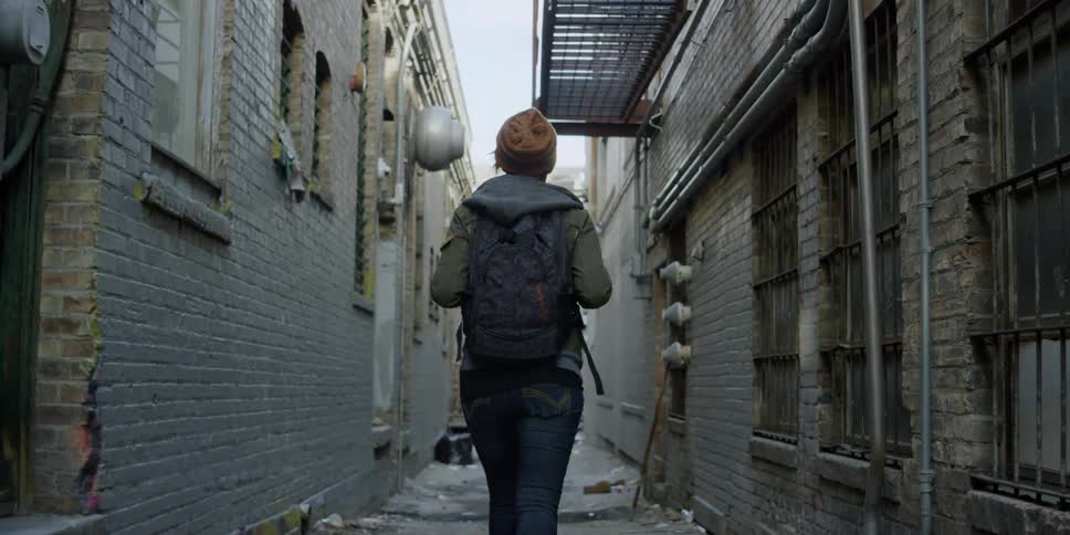 A woman is walking through an alley between brick buildings in daylight