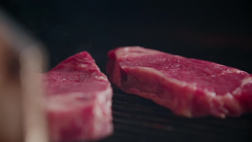 The raw steaks are slowly cooking on the grill