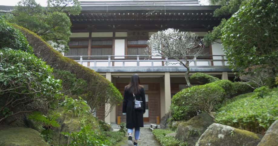 A woman is walking up to a japanese-style building in daylight