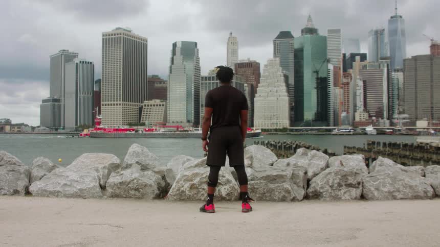 A man is standing at the edge of a river looking at a large city