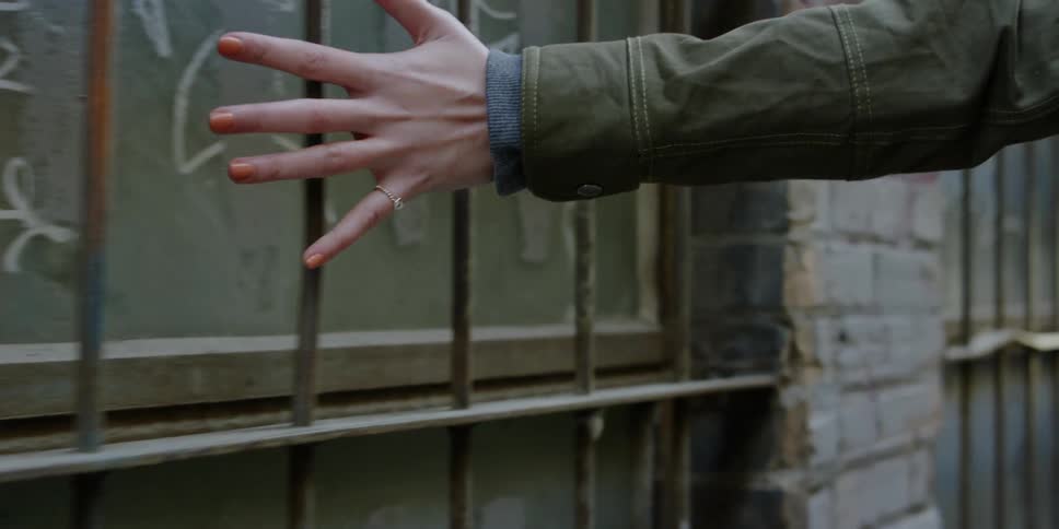 A woman drags her hand along building bricks and grates as she walks