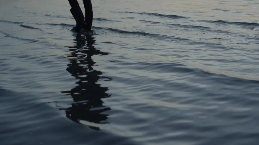 A person wearing boots wades in the surf
