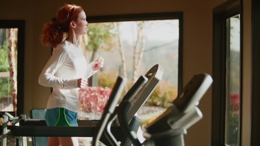 A woman jogs on a treadmill near large windows