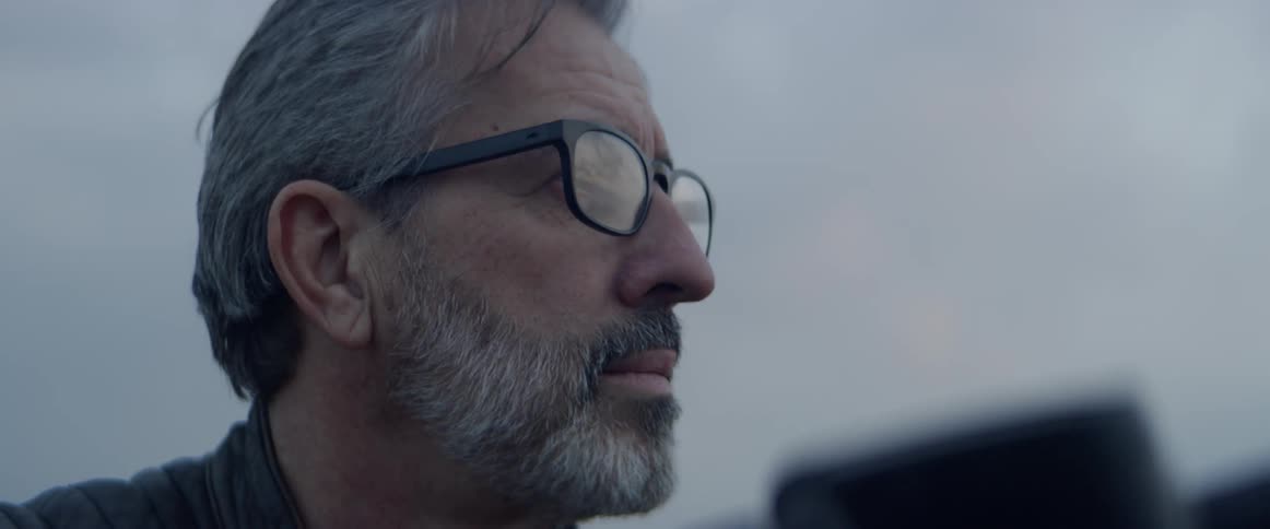 A man wearing glasses looks at something outside
