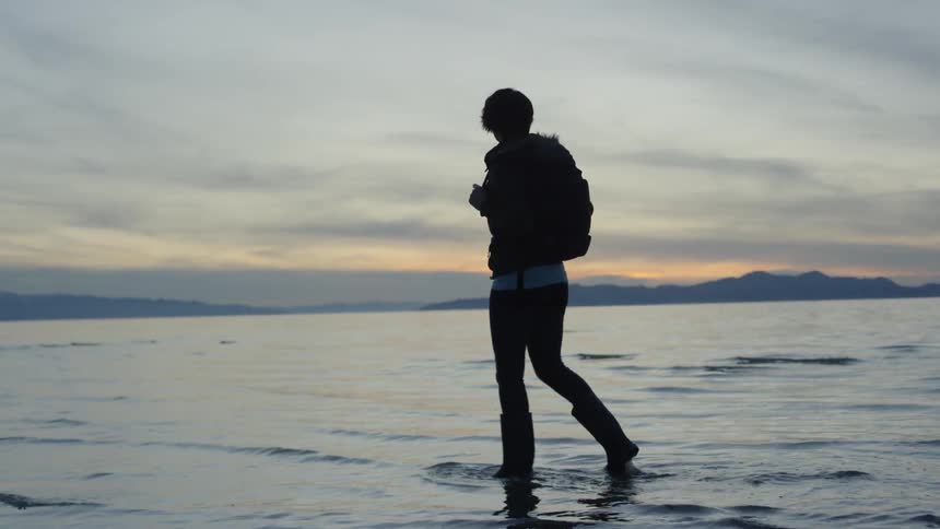 A woman is walking in the water of the beach