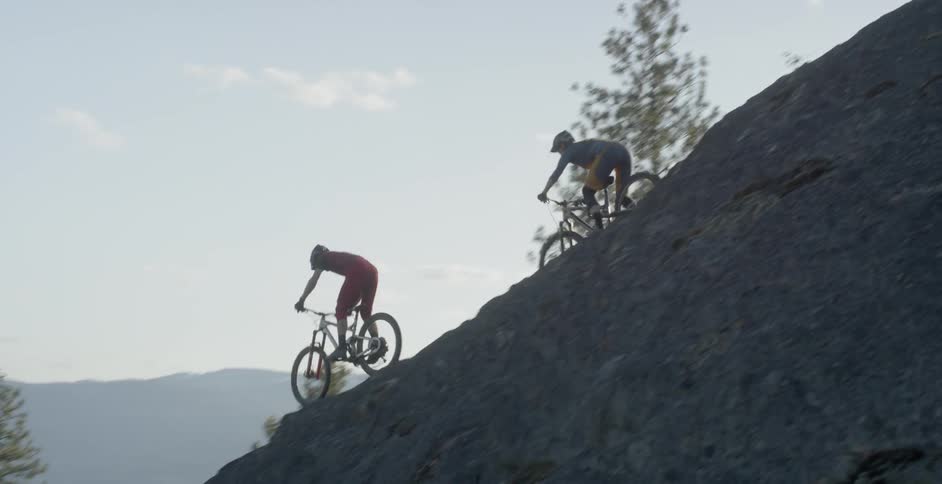 Two people ride mountain bikes down a rocky ridge