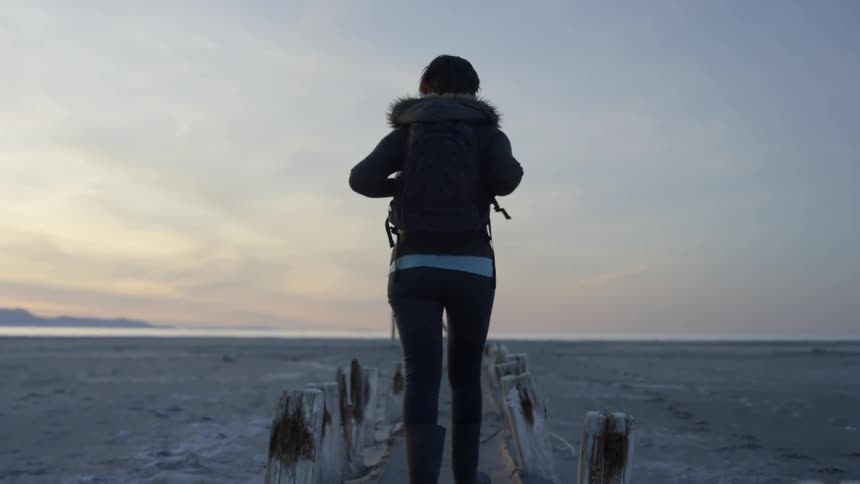 Woman hikes on a beach at sunset