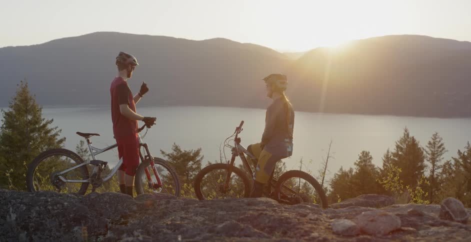 Man and woman with mountain bikes are watching the sunset near lake