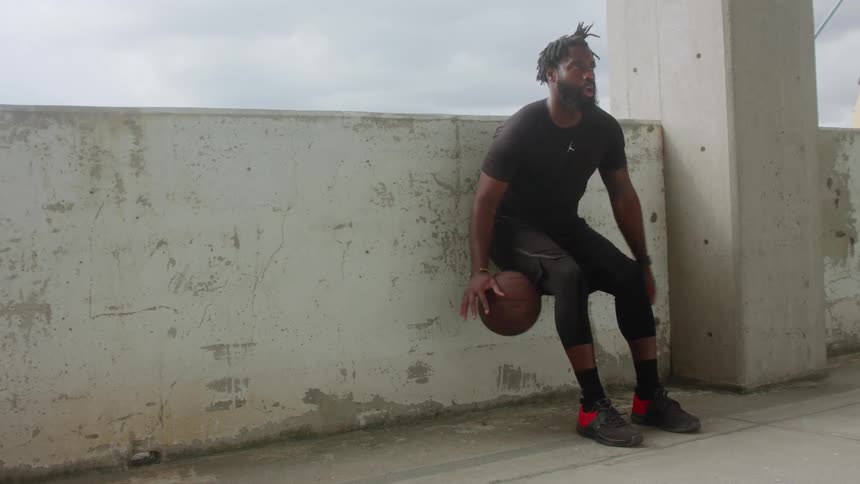 A man leans back against a wall and dribbles a ball