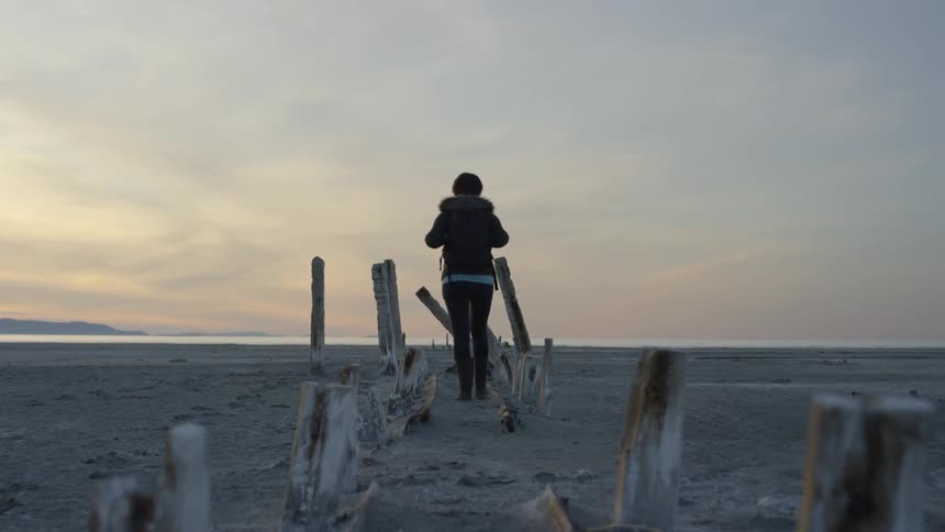 A woman walks down the broken pier on the beach