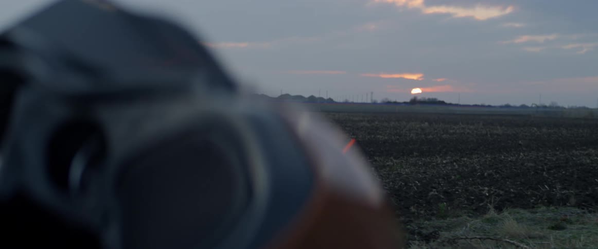 A motorcycle is parked in a rural field at sunset