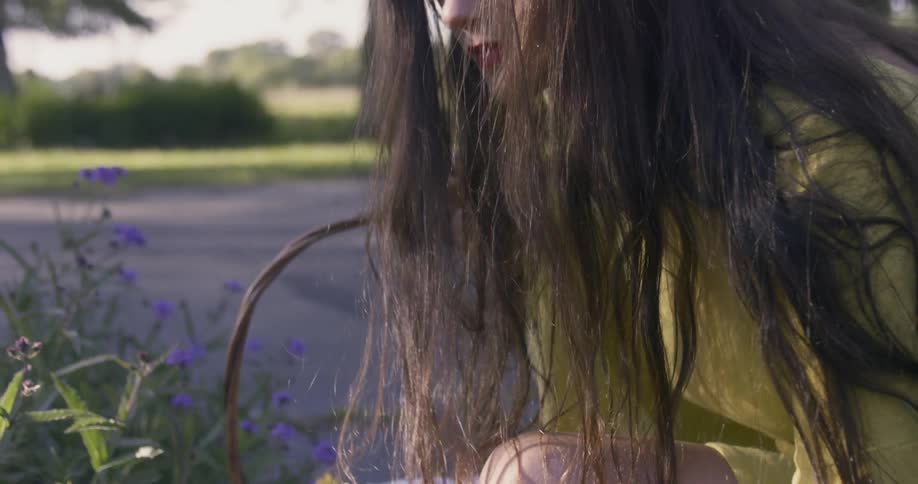Woman carrying a basket sits down near flowers