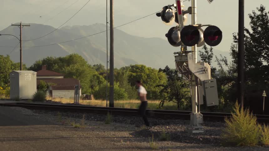 A man runs across train tracks as he pulls on his t-shirt