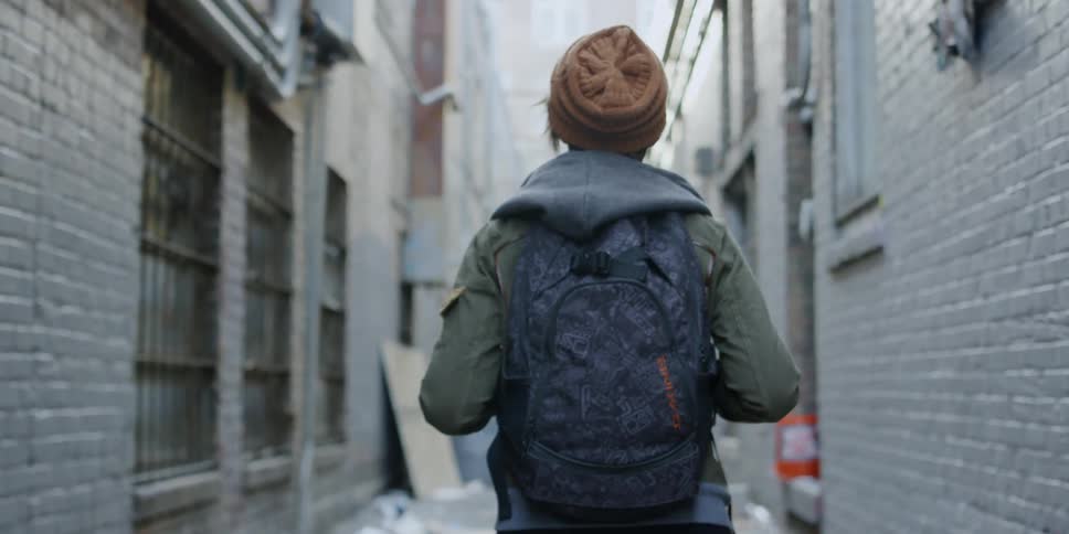 A woman walking down an alley stops walking and turns around